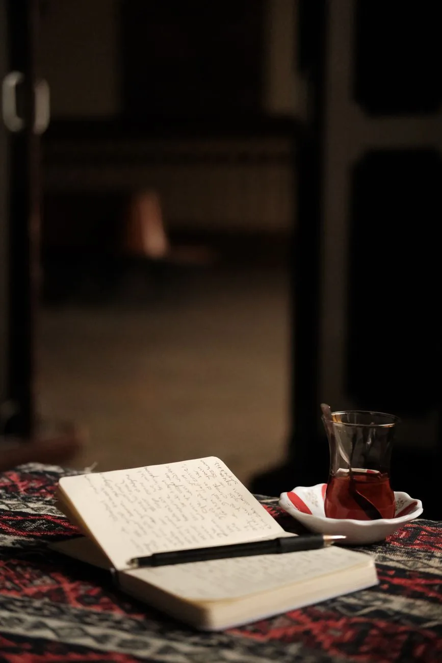 Ahşap bir masada açık duran çizgili defter ve yanında sıcak çay